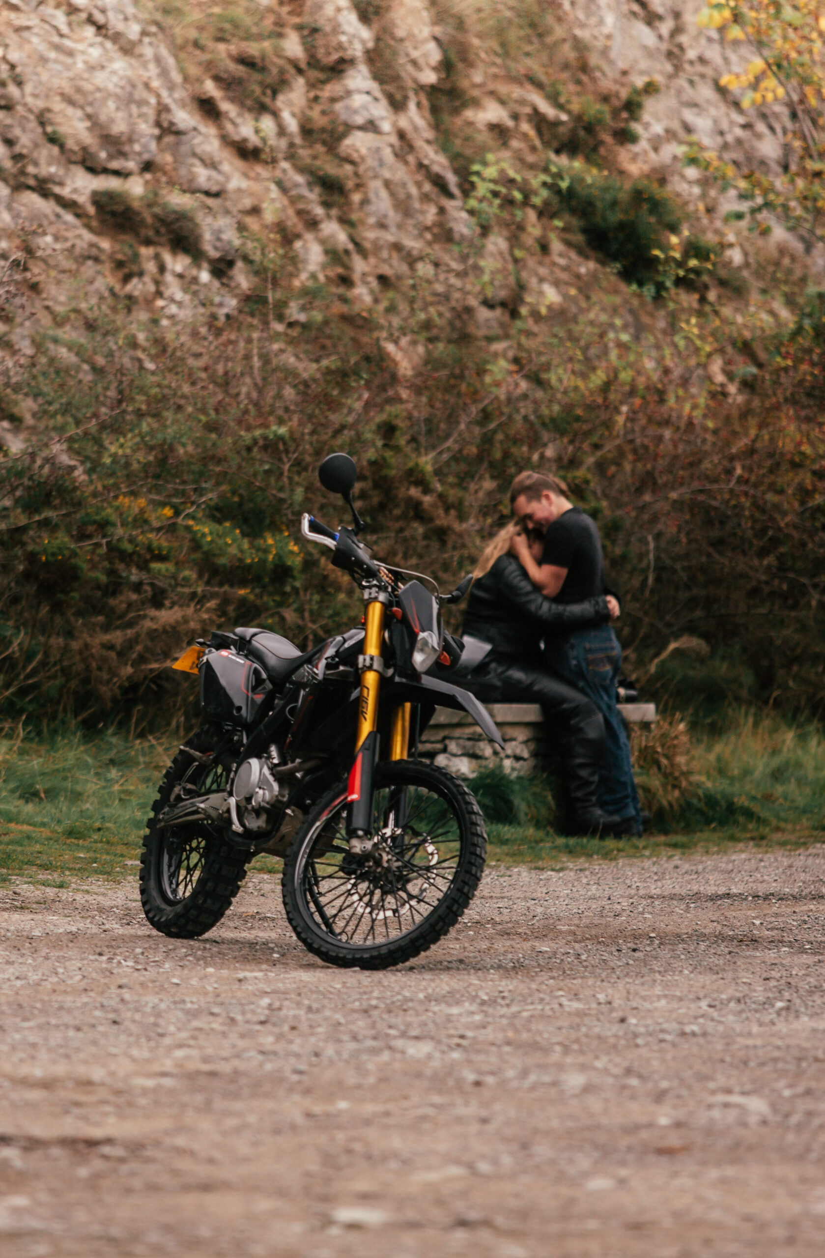 Motorbike and couple sharing a moment after a surprise proposal in the Peak District. Unique and adventurous engagement photography setting.