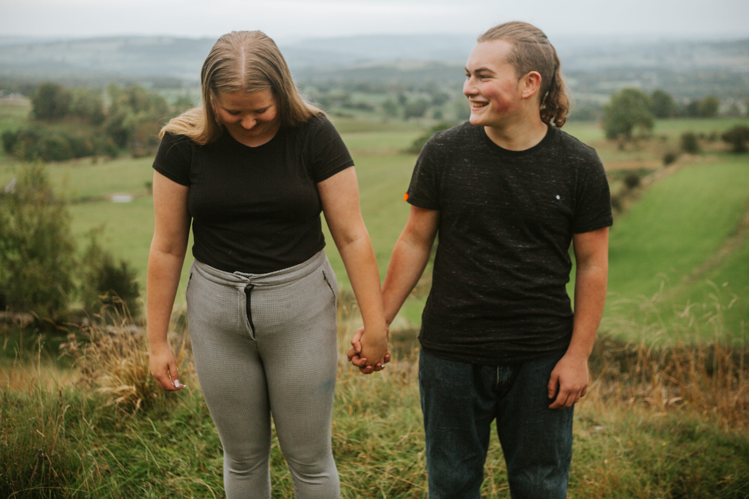 Engaged couple holding hands, smiling naturally during a surprise proposal shoot in the Peak District. Beautiful candid moment captured outdoors.