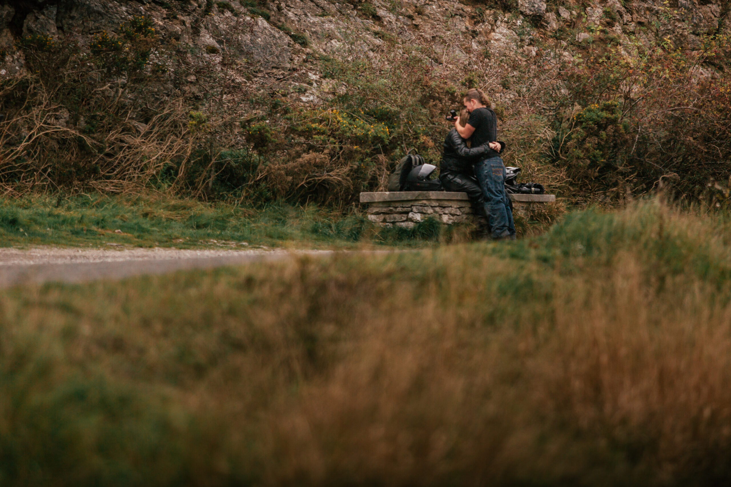 A surprise Peak District proposal captured as a couple sits together under a rocky landscape, highlighting the intimate, natural setting.