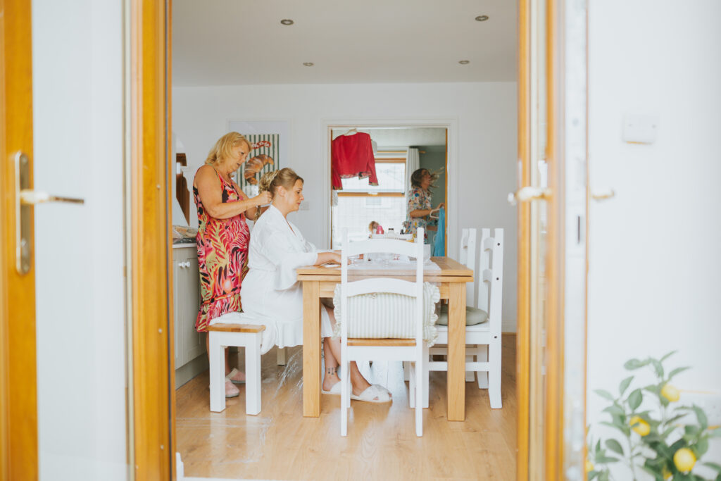 Bride getting ready at home, surrounded by family in a cosy kitchen setting, perfectly capturing the personal, relaxed vibe of a back garden wedding morning.