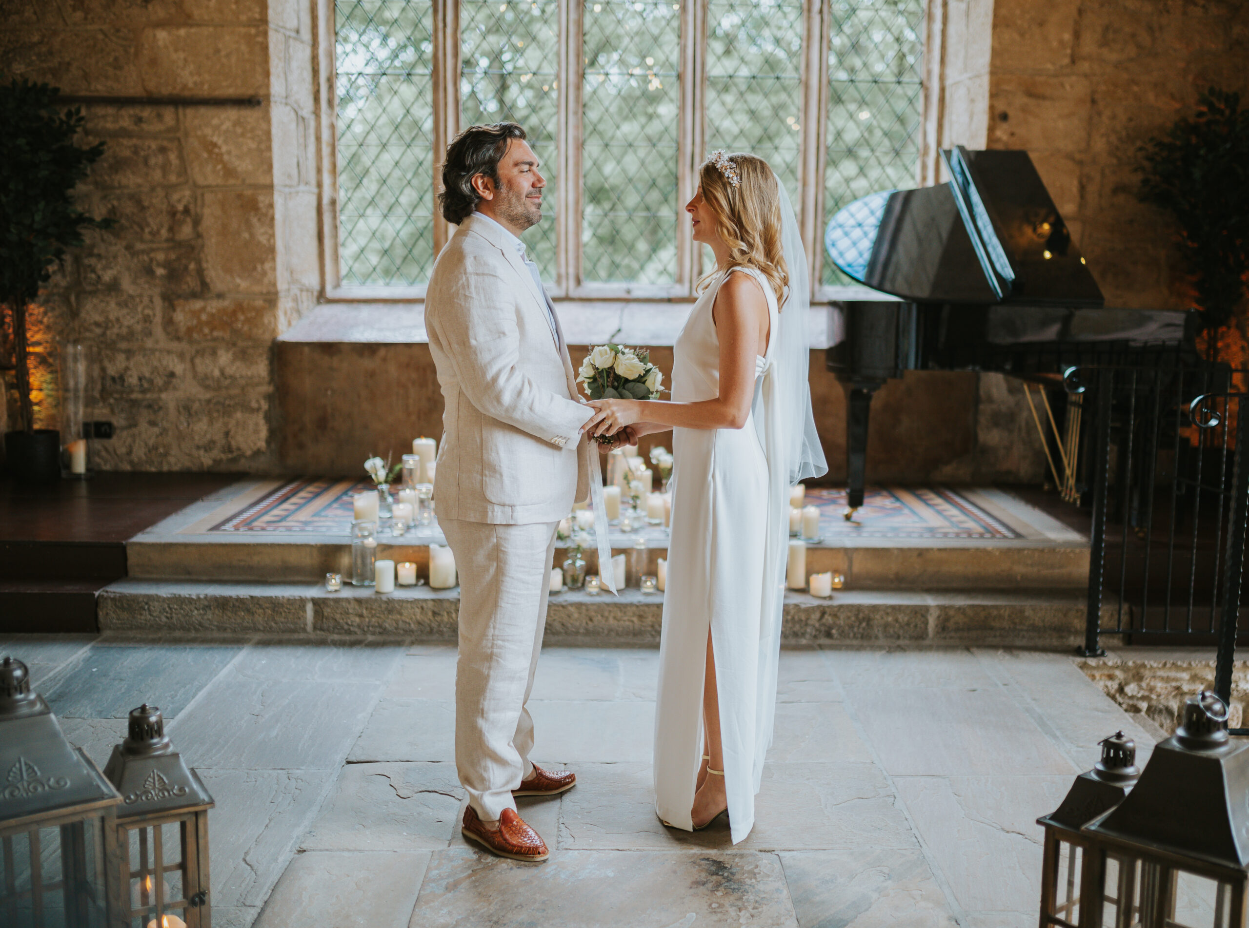 Bride and groom holding hands during their intimate wedding ceremony at The Priests House in Skipton, surrounded by candles and historic stone interiors in the Yorkshire Dales. Perfect setting for natural and romantic wedding photography. Photographed by Slate Cottage Studio.