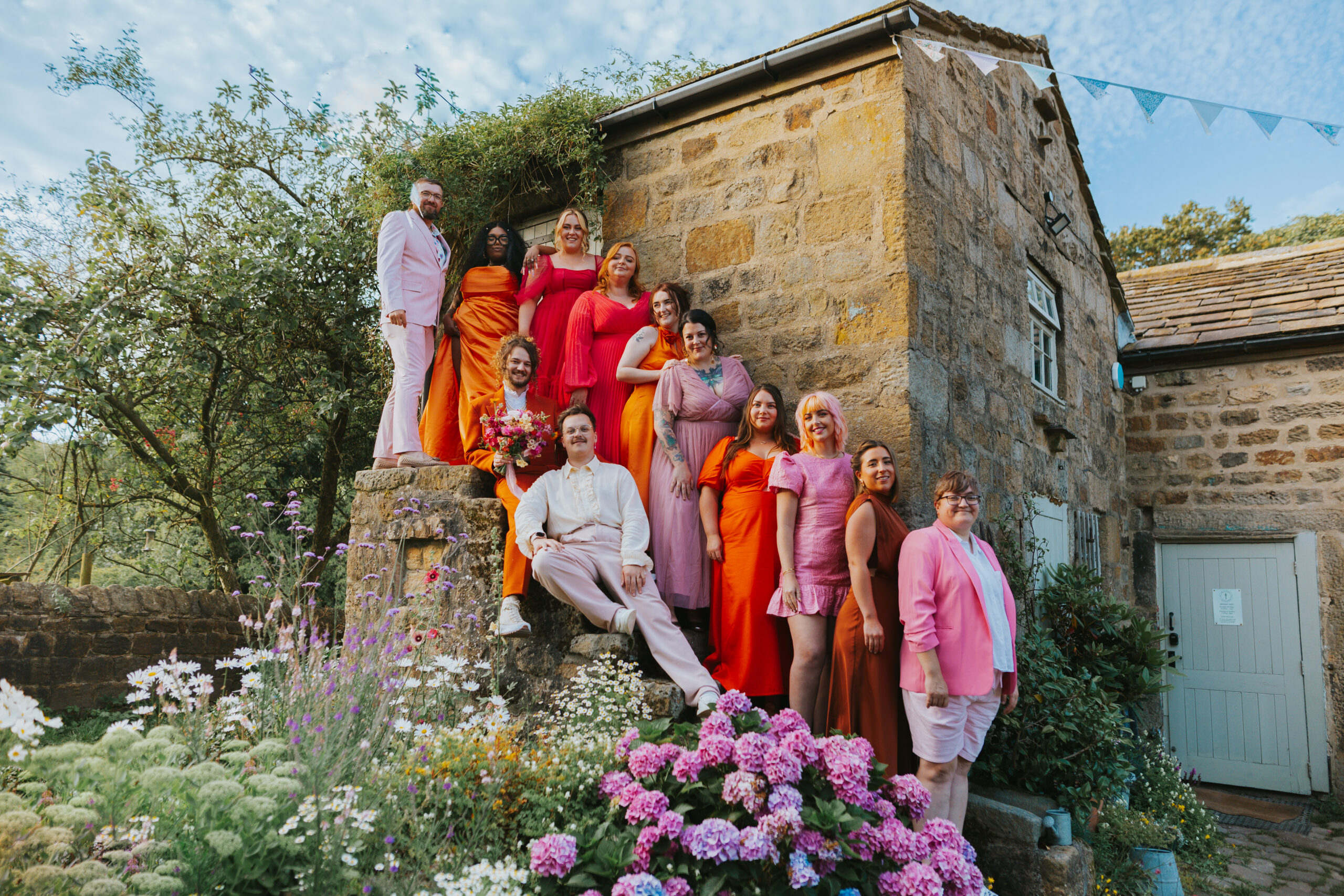 Wedding party group photo wearing bright pink and orange outfits. At the venue, The Chilli Barn, in Otley. Photographed by Slate Cottage Studio.